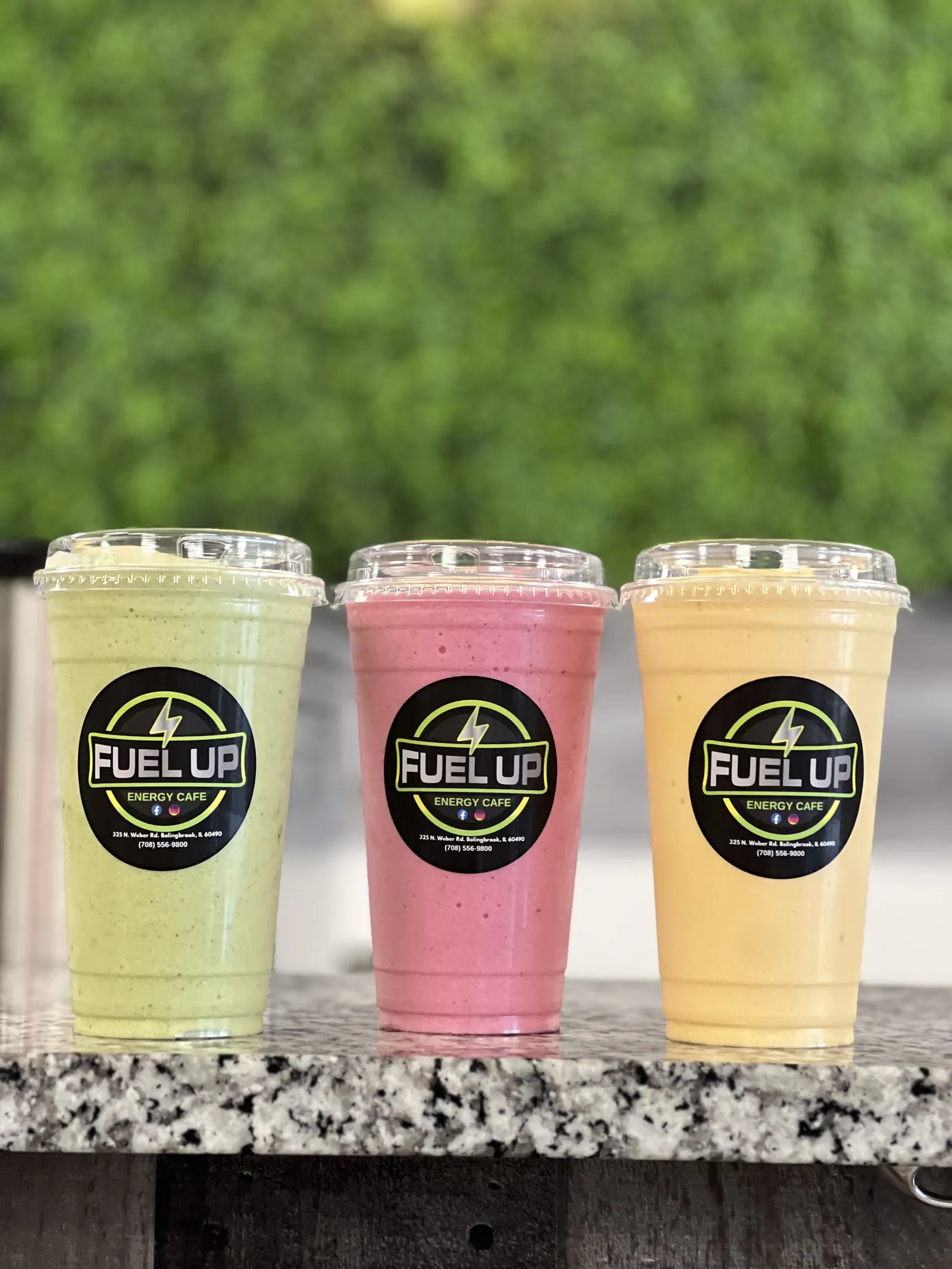 Green, pink and yellow protein smoothies lined up against a greenery wall