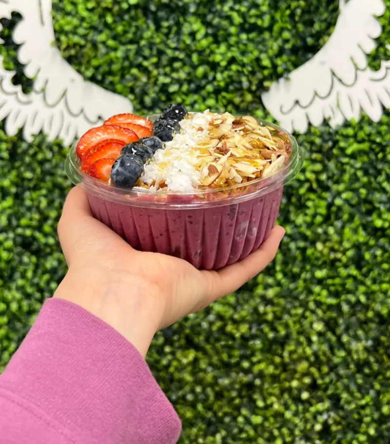 Açaí Bowl with granola, coconut, almonds, strawberries and blueberries held up in the cafe
